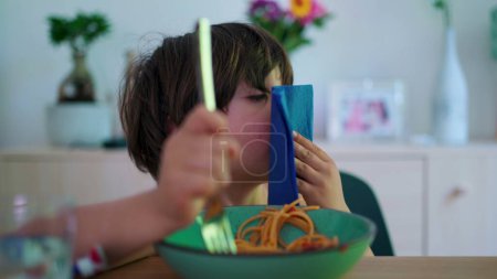 Foto de Niño pequeño limpiando la boca con servilleta mientras come fideos de espagueti para el almuerzo. Niño limpiándose - Imagen libre de derechos