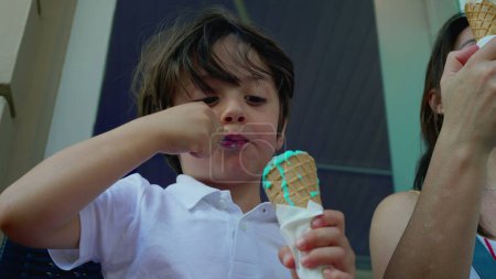 Photo for Concentrated small boy savoring colorful blue ice-cream cone at parlor outside during summer day, close-up of a caucasian male child eating sweet dessert - Royalty Free Image