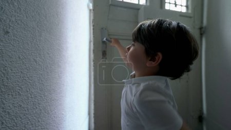 Photo for Little boy opening front door and stepping outdside in city street. Child reaching for door knob and leaving apartment, steps into sidewalk - Royalty Free Image