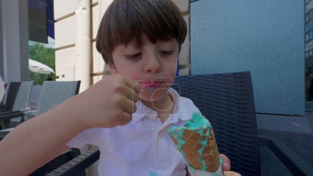 Téléchargez les photos : Petit garçon se livrant avec cône coloré de crème glacée pendant la journée ensoleillée d'été. Enfant manger dessert sucré traiter - en image libre de droit