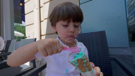 Photo for Small boy indulging himself with colorful ice-cream cone during sunny summer day. Child eating sweet dessert treat - Royalty Free Image
