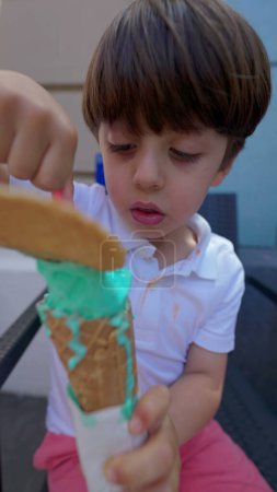Photo for Small boy indulging himself with colorful ice-cream cone during sunny summer day. Child eating sweet dessert treat, vertical video - Royalty Free Image