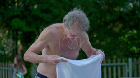 Foto de Hombre mayor poniendo camiseta afuera en un día soleado. Anciano ropa a sí mismo durante el día de verano - Imagen libre de derechos