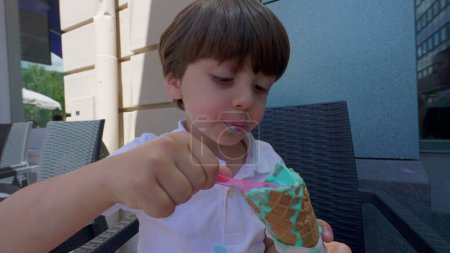 Téléchargez les photos : Petit garçon se livrant avec cône coloré de crème glacée pendant la journée ensoleillée d'été. Enfant manger dessert sucré traiter - en image libre de droit