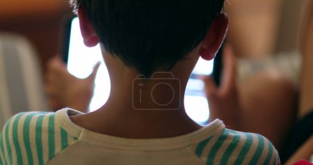 Téléchargez les photos : Arrière de la tête de garçon regardant l'écran de la tablette la nuit avec la lumière bleue rayonnant - en image libre de droit