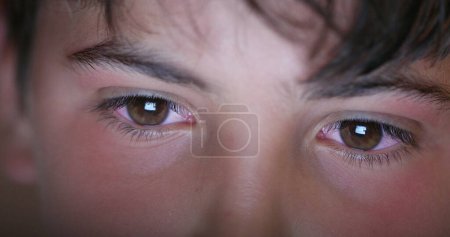 Téléchargez les photos : Boy eyes looking at screen device, blue light glowing from tablet screen. Child macro eye - en image libre de droit