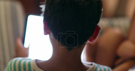 Foto de Back of child head staring at screen device at night - Imagen libre de derechos