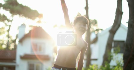 Téléchargez les photos : Boy raising arms in the sky clenching fists in victory and celebration with lens-flare sunlight - en image libre de droit