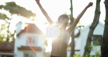 Photo for Boy raising arms in the sky clenching fists in victory and celebration with lens-flare sunlight - Royalty Free Image