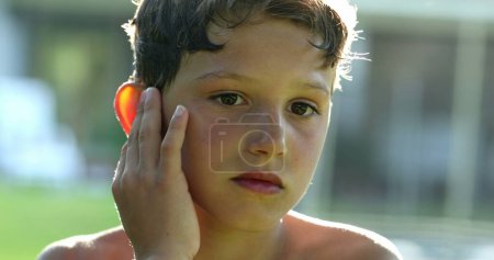 Foto de Boy scratching ear casually outside. Portrait of kid scratches body itching, child touching face - Imagen libre de derechos
