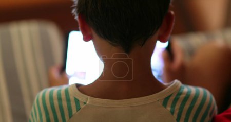 Téléchargez les photos : Boy staring at screen at night. back of Child watching content online - en image libre de droit