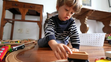 Photo for Small boy playing with car toys on hardwood floor. Child plays by himself with traditional toy on tracks - Royalty Free Image
