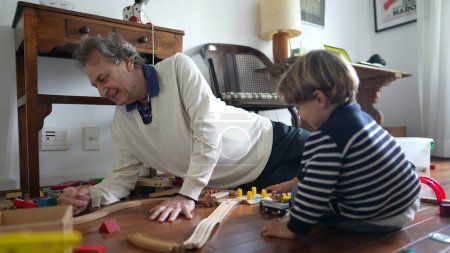Photo for Inter-generational Bonding Over Wooden Train Track Assembly, Grandpa and Grandson Assembling Wooden Train Tracks Together - Royalty Free Image