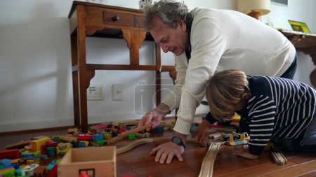 Photo for Grandpa playing with grandson with traditional toys in bedroom floor. Child bonding with grandparent building wooden train tracks together, inter-generational lifestyle - Royalty Free Image