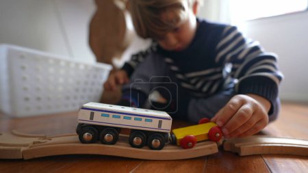 Foto de Niño jugando con juguetes en casa, mano de niño primer plano juega con vagones de ferrocarril retro tradicionales vintage en pistas de madera - Imagen libre de derechos