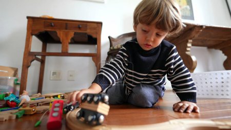 Foto de Niño pequeño jugando con juguetes de coche en el suelo de madera. Niño juega solo con juguetes tradicionales en pistas - Imagen libre de derechos
