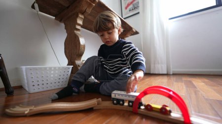Foto de Niño juega con retro vintage tren juguetes en pistas de madera, un niño caucásico jugando solo en casa en el interior - Imagen libre de derechos