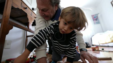 Téléchargez les photos : Grand-père et petit-fils partageant des moments ludiques avec des jouets de train classiques. Aîné et enfant collage sur l'assemblage de voie de train Vintage - en image libre de droit