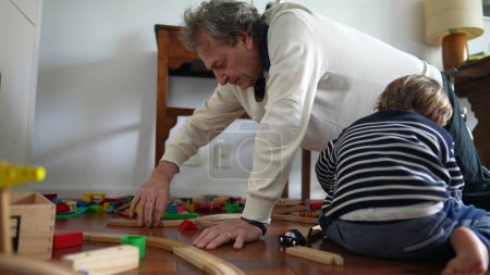 Photo for Grandfather and Grandson Constructing Train Tracks on Hardwood Floor, Elderly Man and Young Boy Building Train Set on Wooden Floor - Royalty Free Image