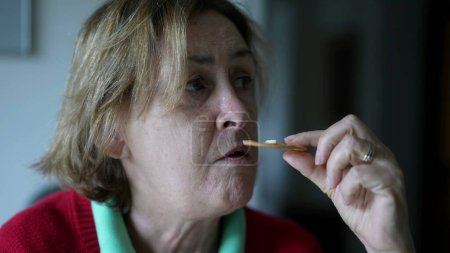 Téléchargez les photos : Femme âgée pensive mangeant des craquelins en pleine réflexion mentale. Gros plan sur le visage d'une dame âgée mange une collation - en image libre de droit