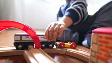 Foto de Primer plano niño mano jugando con juguetes tradicionales en las vías del tren de madera. Niño pequeño empuja carreta retro - Imagen libre de derechos