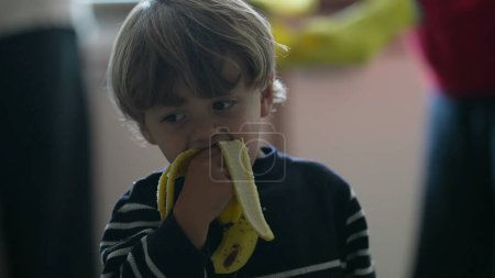 Téléchargez les photos : Petit garçon dégustant une banane, gros plan franc d'un enfant blond ? Enfant blond savourant une collation aux fruits saine - en image libre de droit
