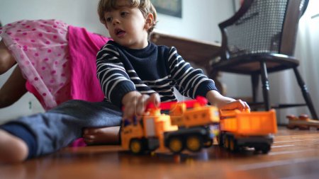 Photo for Small boy clashing trucks together seated on floor. Male child hitting toys plays with objects - Royalty Free Image