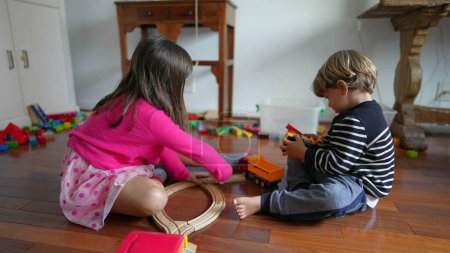 Foto de Niño jugando en casa en el suelo, niño y niña absortos en el juego, hermanos hermano y hermana compartiendo juguetes - Imagen libre de derechos