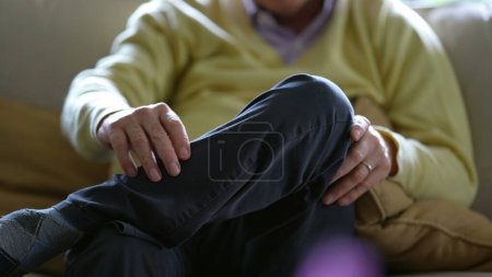 Téléchargez les photos : Homme âgé avec jambes croisées, détail gros plan d'une personne âgée assise sur un canapé à la maison portant un pull et un pantalon jaunes - en image libre de droit