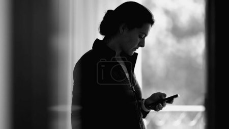 Photo for Monochromatic scene of woman using smartphone device browsing internet on cellphone, person staring at screen - Royalty Free Image