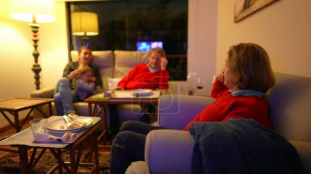 Foto de Personas mayores que interactúan con una hija adulta y un nieto sentados en el sofá por la noche en la sala de televisión, interacción franca con el estilo de vida familiar - Imagen libre de derechos