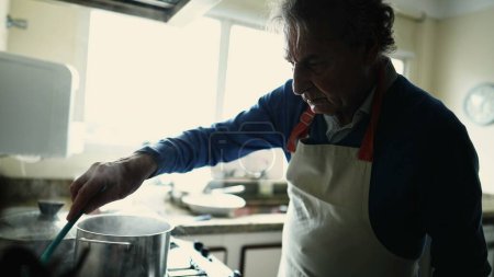 Téléchargez les photos : Homme dans les années 70 Cuisson - Gros plan du chef âgé remuant casserole dans tablier - en image libre de droit