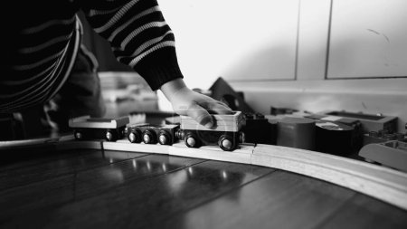 Foto de Niño mano empujando vagón de tren vintage en las vías de madera en monocromo, blanco y negro. Niño jugando con juguete retro - Imagen libre de derechos