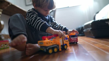 Foto de Niño joven involucrado con juguetes de camiones - Golpear coches de vehículos en el juego enfocado en el hogar, niño caucásico inmerso en el juego - Niño chocando juguetes de camiones juntos en el hogar - Imagen libre de derechos