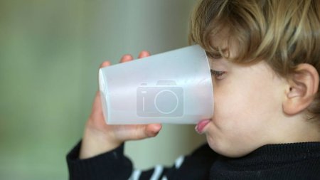 Foto de Niño pequeño bebiendo agua con taza de plástico, cara de perfil de un niño caucásico bebiendo agua, hidratación y estilo de vida saludable - Imagen libre de derechos