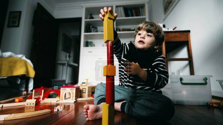 Téléchargez les photos : Petit garçon construisant un bloc de tour, mettant des blocs vintage les uns sur les autres, enfant immergé dans son propre monde, concentré et jouant par lui-même - en image libre de droit