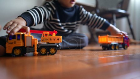 Foto de Un niño chocando con camiones sentados en el suelo. Niño macho golpeando juguetes juega con objetos - Imagen libre de derechos