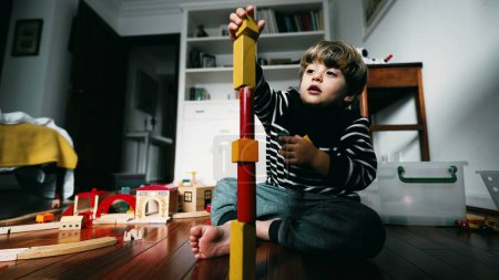 Téléchargez les photos : Petit garçon construisant un bloc de tour, mettant des blocs vintage les uns sur les autres, enfant immergé dans son propre monde, concentré et jouant par lui-même - en image libre de droit