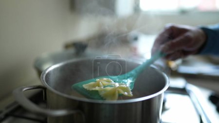 Photo for Close-up hand checking pasta inside metal pan to make sure it is al dente. Cooking carb food procedure on kitchen stove - Royalty Free Image