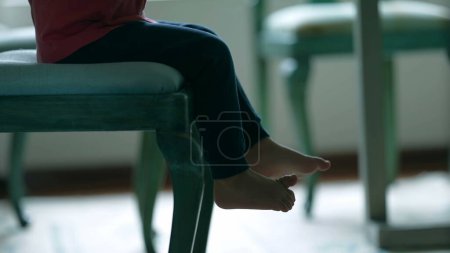 Téléchargez les photos : Jambes et pieds d'enfant assis sur la chaise, mignon petit garçon en attente de nourriture à la table du dîner à la maison - en image libre de droit