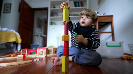 Foto de Niño feliz jugando con bloques de torre. Un niño pequeño poniendo piezas vintage uno encima del otro edificio verticalmente, cayendo. Concepto de ensayo y error - Imagen libre de derechos