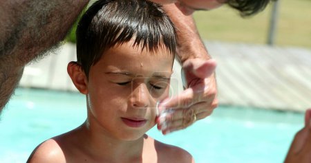 Téléchargez les photos : Père appliquant de la crème solaire sur le visage de l'enfant. Le parent applique un écran solaire sur la peau du garçon - en image libre de droit