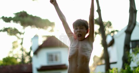 Foto de Child celebrating success and achievement by raising arm in the air. Young boy raises arms and fists in the sky - Imagen libre de derechos
