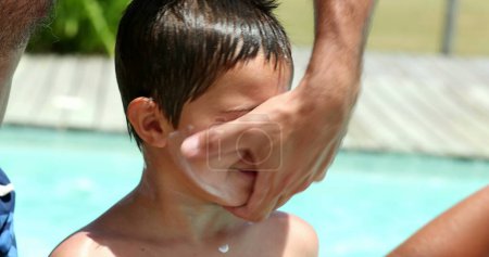 Téléchargez les photos : Père appliquant de la crème solaire sur le visage de l'enfant. Le parent applique un écran solaire sur la peau du garçon - en image libre de droit