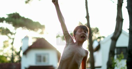 Téléchargez les photos : Child celebrating success and achievement by raising arm in the air. Young boy raises arms and fists in the sky - en image libre de droit