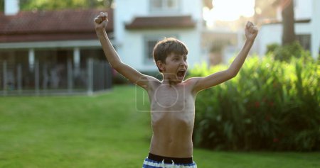 Photo for Child raising arms in the air in celebration. Happy victorious young boy raises arm in the air celebrating - Royalty Free Image