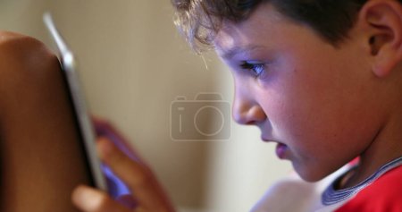Téléchargez les photos : Comprimé pour enfant. numérique natif jeune garçon en utilisant écran tactile dispositif technique jouer jeu vidéo, navigation sur Internet - en image libre de droit