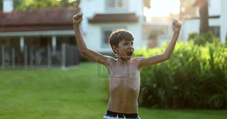 Foto de Child raising arms in the air in celebration. Happy victorious young boy raises arm in the air celebrating - Imagen libre de derechos