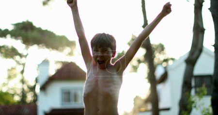 Foto de Child celebrating success and achievement by raising arm in the air. Young boy raises arms and fists in the sky - Imagen libre de derechos