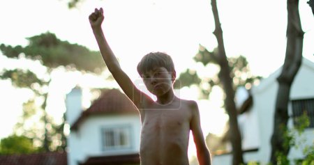 Téléchargez les photos : Child in victory stand raising fist in the air celebrating achievement and success with arm raised to the sky - en image libre de droit